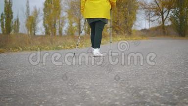 在秋天的森林里做北欧行走的高级妇女。 在秋天的小径上进行北欧步行比赛。 退休人士健康
